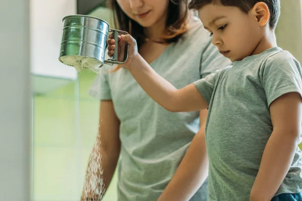 Selective focus of toddler boy holding baking sieve with flour near mother — Stock Photo