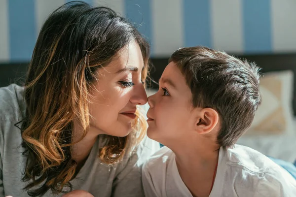 Vista lateral da mãe feliz e filho da criança bonito olhando um para o outro no quarto — Fotografia de Stock