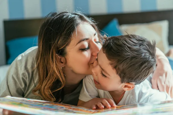 Atraente mãe beijos bochecha de bonito criança menino em casa — Fotografia de Stock