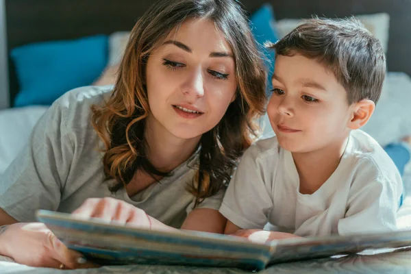 Selective focus of attractive mother and happy toddler boy looking at book — Stock Photo