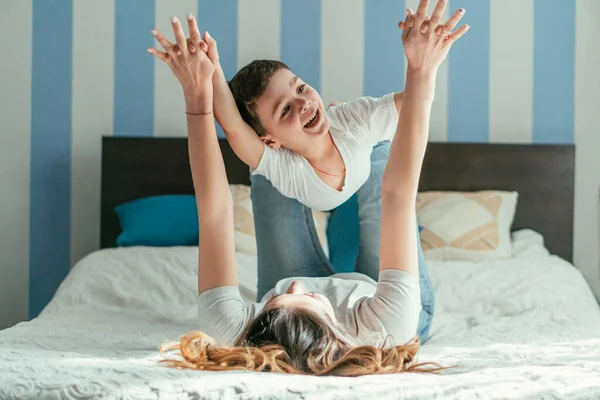 Selective focus of mother lying on bed and holding hands with toddler son while playing in bedroom — Stock Photo