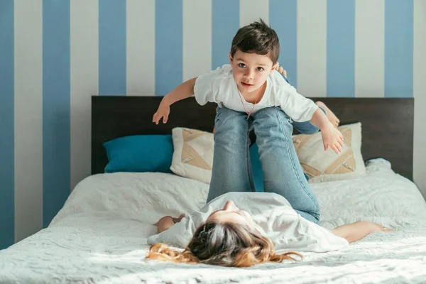 Selective focus of toddler boy with outstretched hands lying on legs of mother in bedroom — Stock Photo