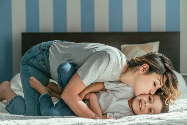 Madre baciare guancia di carino bambino figlio sul letto — Foto stock
