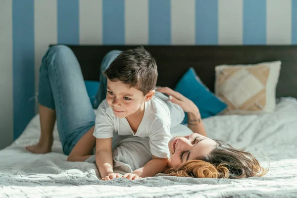 Alegre madre acostada en la cama con lindo niño en el dormitorio - foto de stock