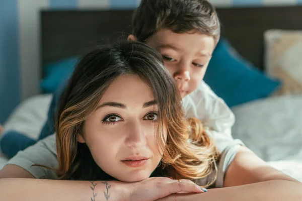 Selective focus of tattooed woman looking at camera near toddler son at home — Stock Photo