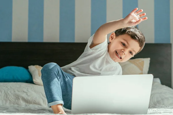 Foco seletivo de criança feliz menino acenando a mão enquanto tem chamada de vídeo em casa — Fotografia de Stock