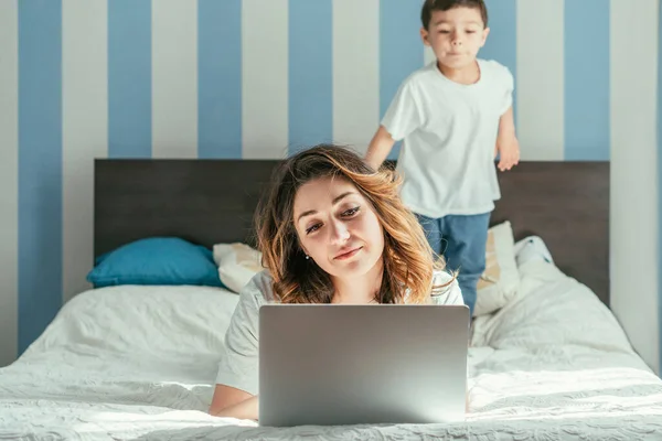 Selective focus of freelancer working from home near toddler son in bedroom — Stock Photo