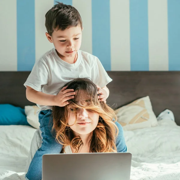 Entzückender Kleinkind Junge berührt Haare einer freiberuflichen Mutter im Schlafzimmer — Stockfoto