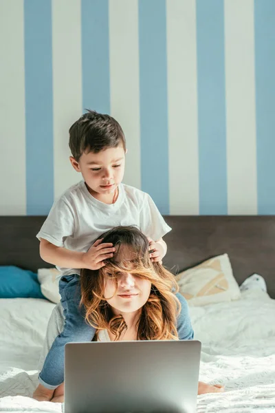 Tout-petit garçon toucher les cheveux de la mère pigiste dans la chambre — Photo de stock