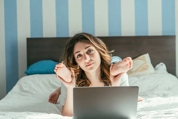 Freelancer tocando las piernas de su hijo pequeño cerca del portátil en la cama - foto de stock