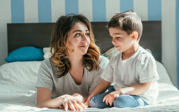 Atractiva mujer mirando a su hijo pequeño en el dormitorio - foto de stock