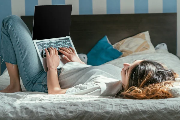 Селективный фокус фрилансера, лежащего на кровати с помощью ноутбука с чистым экраном — стоковое фото