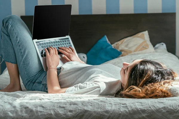 Enfoque selectivo del freelancer acostado en la cama con el ordenador portátil con pantalla en blanco — Stock Photo