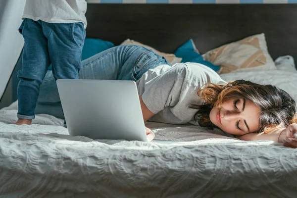 Fuoco selettivo di collaboratore esterno che si trova su letto vicino a computer portatile e figlio del bambino — Stock Photo