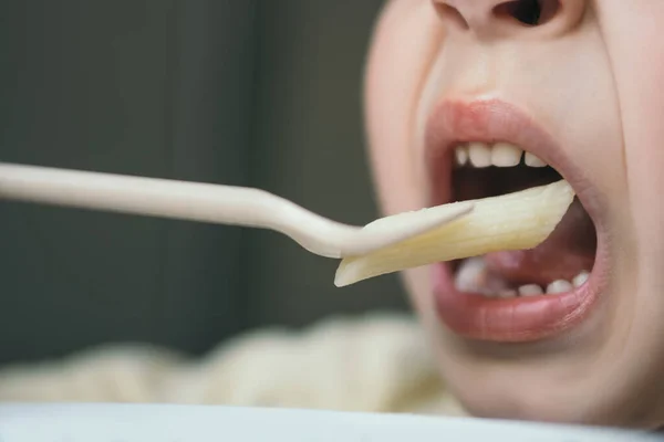 Close up view of little boy eating penne pasta with fork — Stock Photo