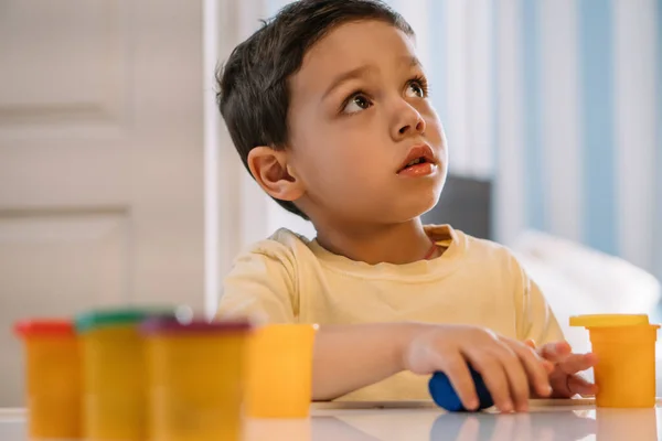 Selective focus of thoughtful boy looking up while holding colorful plasticine — Stock Photo