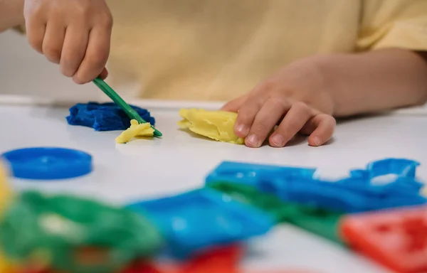 Vista ritagliata del bambino che taglia plastilina colorata con spatola — Foto stock