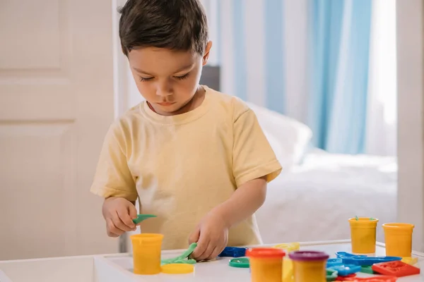 Bonito, menino atencioso segurando vara enquanto esculpindo com plasticina colorida — Fotografia de Stock