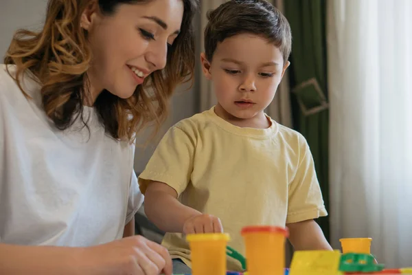 Sonriente madre con adorable hijo mirando coloridos recipientes con plastilina - foto de stock