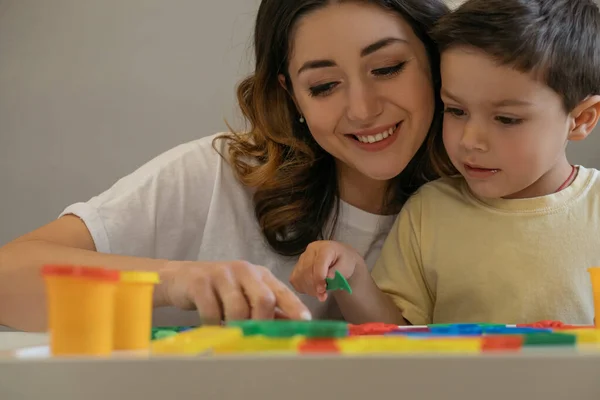 Smiling woman pointing with finger at play clay while attentive son holding spatula — Stock Photo