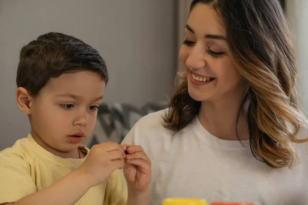 Mulher alegre olhando para filho esculpir figura de plasticina — Fotografia de Stock