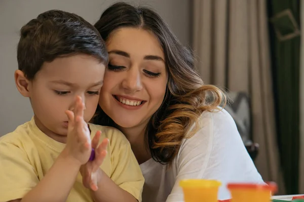 Mulher feliz abraçando adorável filho esculpir figuras de plasticina — Fotografia de Stock