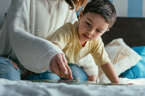 Vista parcial de la mujer jugando juego de mesa junto con el niño lindo en la cama - foto de stock