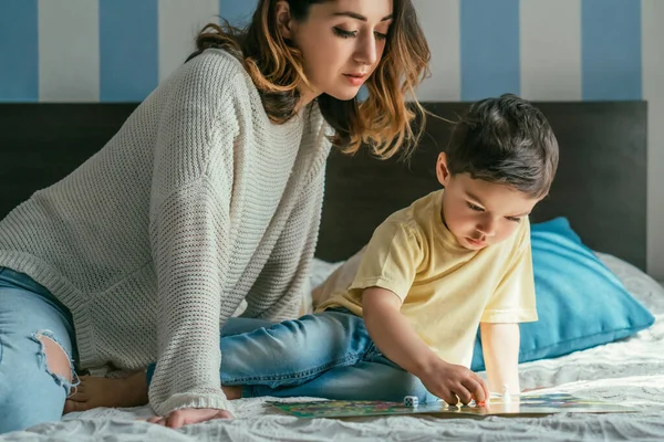 Schöne Frau schaut Sohn beim Brettspiel im Bett an — Stockfoto