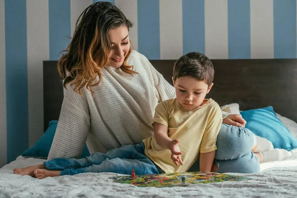 Sorrindo mãe com filho atento jogando jogo de tabuleiro na cama — Stock Photo