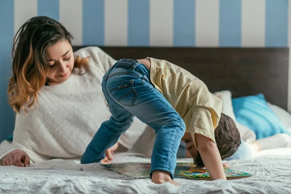 Carino ragazzo avendo divertimento su letto vicino felice madre — Foto stock