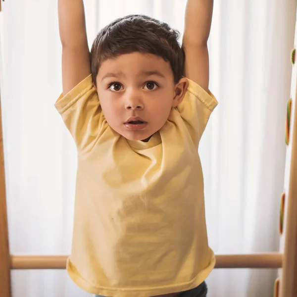 Adorable child hanging on horizontal bar while exersicing in home gym — Stock Photo