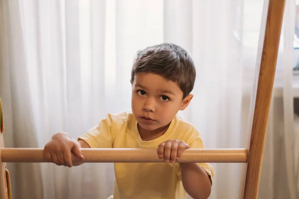 Adorable kid looking at camera while touching ladder of home gym — Stock Photo