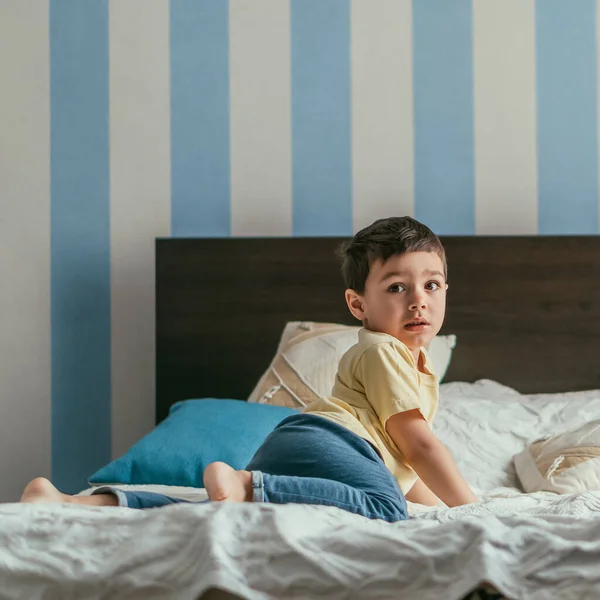 Garoto bonito olhando para a câmera enquanto rastejando na cama em casa — Fotografia de Stock