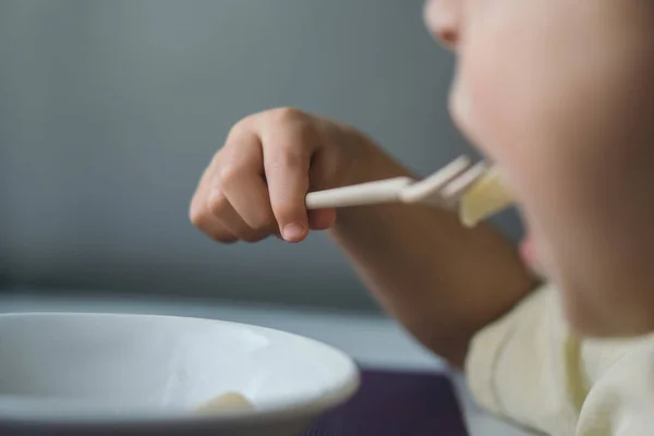Обрезанный вид маленького мальчика за ужином во время еды пасты с вилкой — стоковое фото