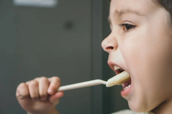 Вид сбоку на восхитительного мальчика, обедающего во время еды пасты с вилкой — стоковое фото