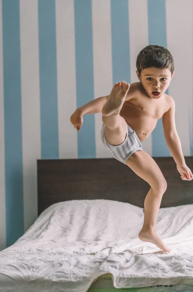 Cute boy having fun while jumping and kicking with leg on bed — Stock Photo