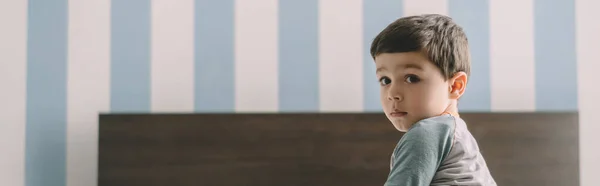 Horizontal image of cute, serious boy looking at camera while sitting in bedroom — Stock Photo