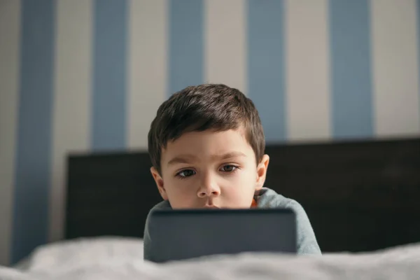 Selektiver Fokus des entzückenden Jungen, der im Schlafzimmer auf das Smartphone schaut — Stockfoto