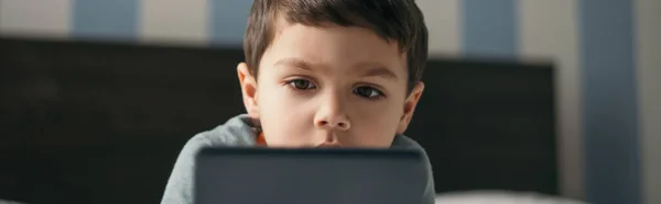 Selective focus of adorable boy looking at smartphone in bedroom, horizontal image — Stock Photo