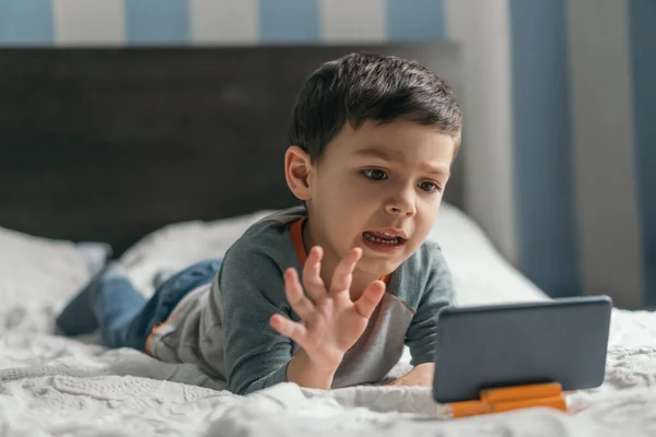 Aufgeregter, entzückender Junge gestikuliert, während er Cartoon auf Smartphone im Schlafzimmer sieht — Stockfoto