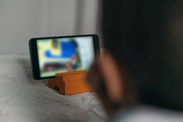 Selektiver Fokus des Kindes beim Zeichentrickgucken auf dem Smartphone, während es im Bett liegt — Stockfoto