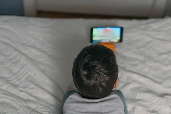 Вид сверху на ребенка, смотрящего онлайн урок во время лежания на кровати — стоковое фото