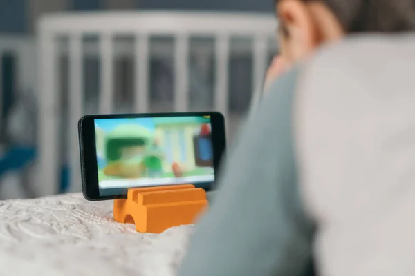 Selective focus of boy watching online lesson on smartphone while lying on bed — Stock Photo
