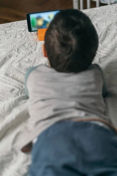 Selektiver Fokus eines kleinen Jungen, der Webinar auf dem Smartphone verfolgt, während er im Bett liegt — Stockfoto