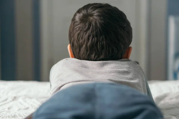 Back view of little brunette boy lying on bed at home — Stock Photo