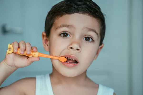 Mignon petit garçon regardant caméra tout en brossant les dents dans salle de bain — Photo de stock