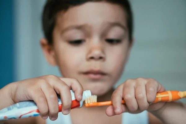 Enfoque selectivo del niño diligente aplicando pasta de dientes en el cepillo de dientes - foto de stock