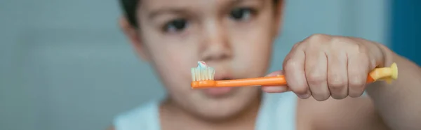 Selektiver Fokus des netten Jungen, der auf Zahnbürste mit Zahnpasta blickt, horizontales Bild — Stockfoto