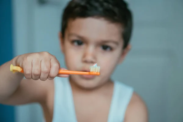 Enfoque selectivo de chico lindo mirando cepillo de dientes con pasta de dientes - foto de stock