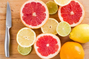 Taze narenciye (limon, limon, greyfurt, portakal) ahşap kesme tahtası üzerinde metal bir bıçakla dilimlenmiş, sayfa görünümü